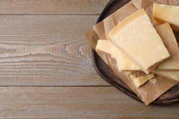 Pieces of delicious parmesan cheese on wooden table, top view. Space for text