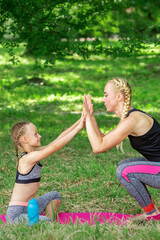 Fototapeta premium Mother and daughter doing sports exercises on the mat in the park outdoor