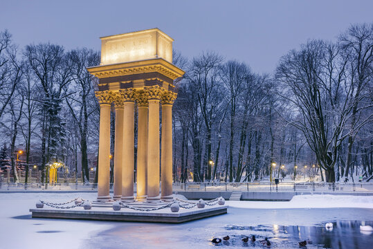 Illuminated General Bem Monument in Tarnow, Poland. Magical Winter Snowfall in City Park and Pond at Twilight