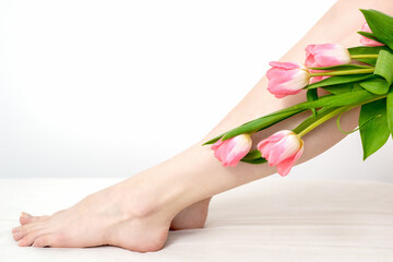Beautiful slim smooth woman's legs with tulips flowers on white background
