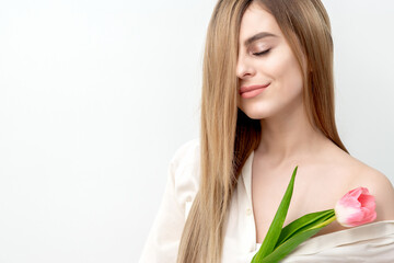 A portrait of a happy young caucasian woman with closed eyes and one pink tulip against a white background with copy space