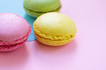 Fototapeta na wymiar Green, pink and yellow macaroons french biscuits with fillings on blue and pink backgrounds. Traditional french pastry