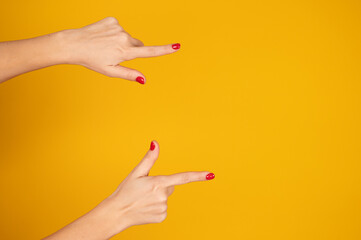 Female hands close-up, long index finger pointing at something. Gesture of direction. Yellow background. Copy space. Hand sign concept