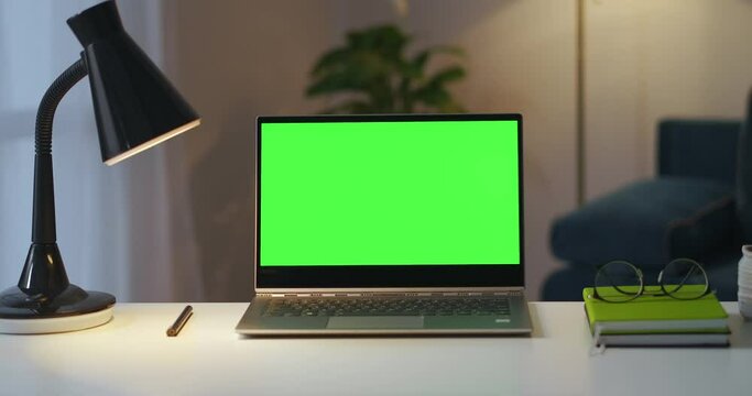working place of writer or freelancer in apartment, laptop with green screen for chroma key, books and lamp on table
