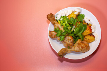 Fried chicken thighs with fried potatoes and greens on a pink background