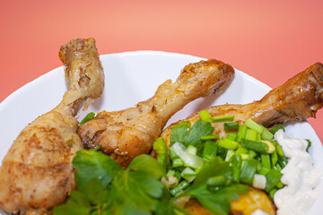 Fried chicken thighs with fried potatoes and greens on a pink background