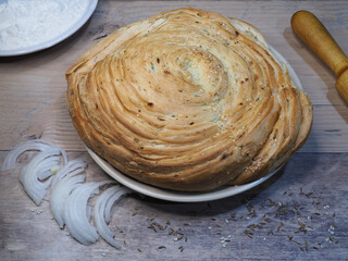 Uzbek flatbread fatir with onion, sesame seeds and cumin on a wooden background, closeup, flat layout. Traditional Asian pita made of wheat flour, puff pastry with spices. Bakery of oriental cuisine