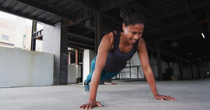 African american woman exercising doing push ups in an empty urban building