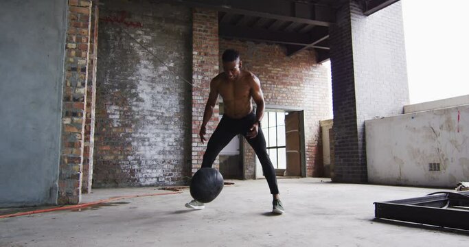 Shirtless african american man exercising with medicine ball in an empty urban building