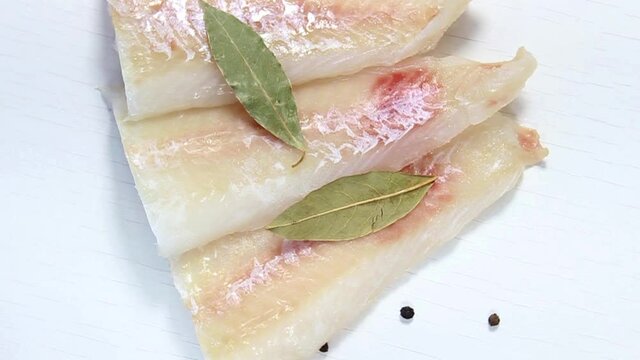 Raw pollock fillet sprinkled with salt, pepper and bay leaf. Top view, selective shot.