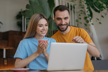 Young couple using laptop computer, shopping online at home. Smiling  man and woman make video conference call, communication online. Bloggers streaming video 