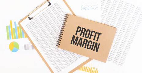Text PROFIT MARGIN on brown paper notepad on the table with diagram. Business concept