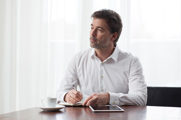 Handsome serious man taking notes looking away. Teleworking. Telecommuting