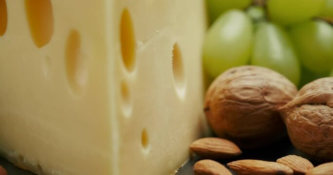 Close up part of Medium hard cheese head edam gouda parmesan on wooden board, with nuts and grapes rotaiting on the plate.