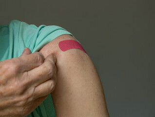 Senior caucasian man holding up shirt sleeve to show the bandaid after coronavirus vaccine shot in...
