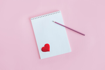 Notebook with blank page, pencil and red heart on a pink background.
