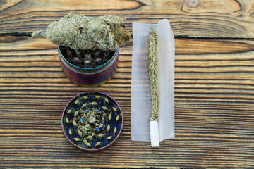Grinder with crushed cannabis flowers and not twirled jamb on the background of a funky wooden table