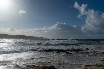 Coastline with rocks, a blue sky and rough incoming waves with sea spray during a storm