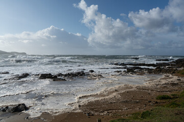 Coastline with rocks, a blue sky and rough incoming waves with sea spray during a storm