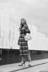 Elegant woman walking city street. Fashion fall autumn look. Pretty caucasian blonde stylish girl wearing blue jeans, wine red pullover and squared wool coat. Female with makeup and wavy blonde hair