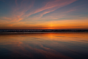 Reflection of blood red sunset on the wet sand on the beach and dark horizon line