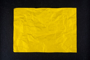 Yellow crumpled sheet of paper on a dark wall.