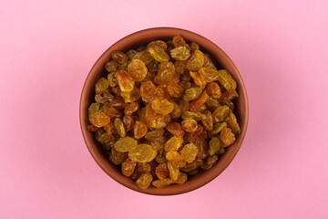 Raisins in a bowl on a pink background.