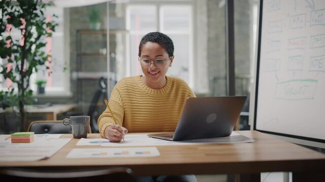 Portrait of Young Latin Marketing Specialist in Glasses Working on Laptop Computer in Busy Creative Office Environment. Beautiful Diverse Multiethnic Female Project Manager is Browsing Internet.