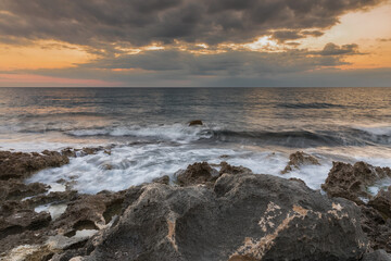 The waves take away the foam and its fish; the sea gives a glimpse of the pointed rock, reflects an orange and red sunset and the gray clouds make a glimpse of an oncoming storm.