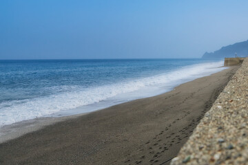 A sea of ​​a thousand shades of blue, a beach of round and gray stones in volcanic lava.  The mountains in the background.
