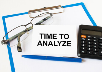 A business card with text Time To Analyze lying on a clipboard with a blue pen eyeglasses and a...