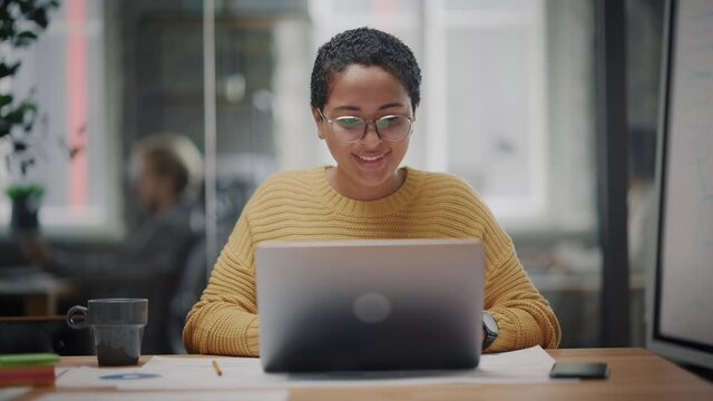 Portrait of Young Latin Marketing Specialist in Glasses Working on Laptop Computer in Busy Creative Office Environment. Beautiful Diverse Multiethnic Female Project Manager is Browsing Internet.