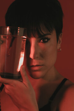 Portrait of a woman looking at camera while holding a glass of water in studio