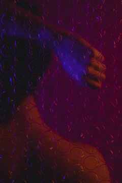 Naked back of a woman raising her hand behind plastic bubble wrap