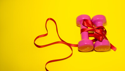 Two pink dumbbells are tied with a red ribbon. Valentine's day concept, sport for lovers. Healthy lifestyle, giving gifts, love sports. Fashionable color yellow
