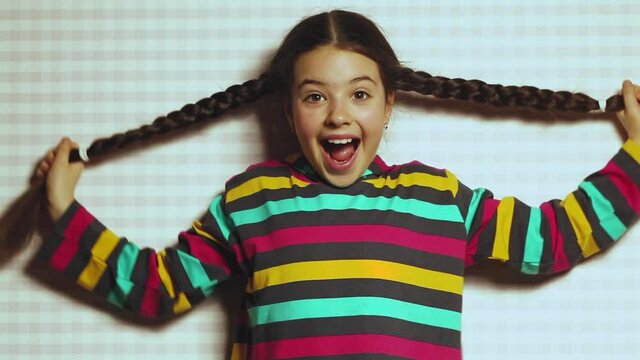 A beautiful dark-skinned little girl in a bright striped sweatshirt laughs, covering her face with her pigtails. Cute funny emotional teenager. Shy girl.
