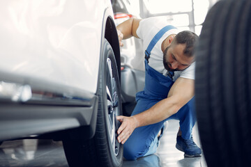 Naklejka premium Wrker in a car salon. Expert checks the car. Man in a blue uniform.