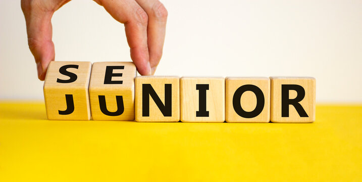 From junior to senior symbol. Businessman turns cubes and changes the word 'junior' to 'senior'. Beautiful yellow table, white background, copy space. Business and junior or senior concept.
