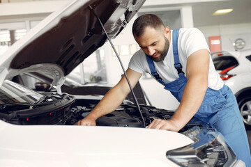 Wrker in a car salon. Expert checks the car. Man in a blue uniform.