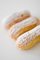 Home made cake eclairs on a white table with sugar powder. Traditional eclairs, profitroles classic, eclairs french.