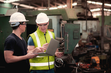 Two Caucasian Factory Technician Engineer is working with machine in industrial plants and check the operation and maintenance program of the machine in the laptop
