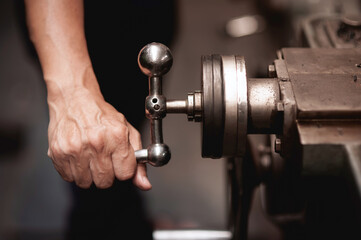 Close-up of a mechanician's hand covered is turning on the lathe handle To control the operation of the machine