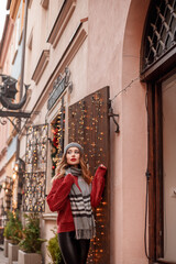 Obraz na płótnie Canvas Outdoors lifestyle fashion portrait of stunning blonde young woman. Wearing stylish knitted hat and scarf. woman walking at christmas city market with lights, decorations and carousel on background.