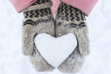Women's hands in woolen mittens hold a snowy heart. Symbol of love. Valentine's Day concept. Selective focus, close-up