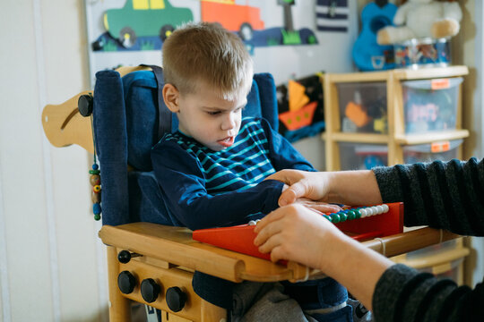 Activities For Kids With Disabilities. Preschool Activities For Children With Special Needs. Boy With With Cerebral Palsy In Special Chair Play With Mom At Home.