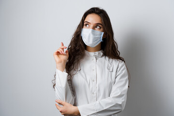 Doctor pointing left side. Young woman doctor in medical mask and medical robe. Empty place for text of advert.