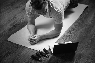 50 year old man performs exercises lying on mat at home looking at computer