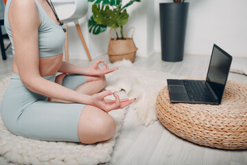 Adult mature woman doing yoga at home living room with online tutorials on laptop