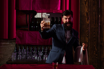 Waiter bartender in bar. Handsome bearded barman with long beard and mustache with serious face made alcoholic cocktail in vintage suede leather on purple red bar background.