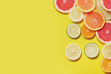 Slices of citrus fruits on yellow background.